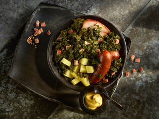 Grünkohl mit Kartoffeln, Kochwurst und Senf auf schwarzem Metallfond