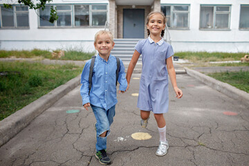 Back to school. Happy siblings with backpacks, elementary school kids, running from the school...