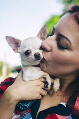 The girl holds a mini chihuahua in her arms. Kissing your pet. The dog and the owner are dressed in the same color. Clothes for animals. Love and care for four-legged pets.