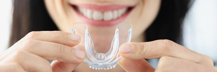 Woman holding plastic mouth guard for bruxism treatment closeup