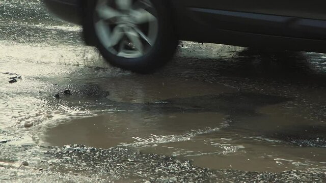 Uneven potholes on the asphalt, damaged road infrastructure after rain. Cars drive slowly along the road with pits and puddles. Asphalt in violation of technology. Taxpayer money is wasted. UHD 4K.