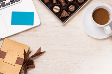 Glass of chocolate milk and variety chocolates  on table with gift box and laptop.