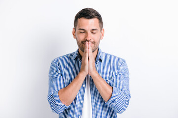 Peaceful mind, harmony. Portrait of man in casual closes holding hands cupped and praying with grateful expression, practicing yoga meditation. Indoor studio shot isolated on white background