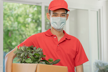 Fototapeta na wymiar Cargo company, asian man, male wearing mask protect pandemic covid-19 in blue uniform, unpacking carton and show plant pot before packing in cardboard box. Moving, preparing in new house, relocation.