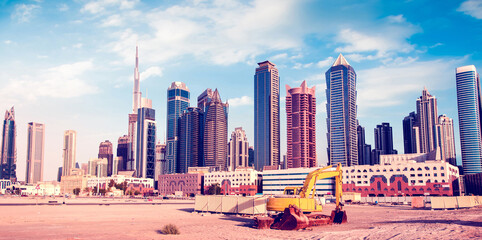 Bulldozer on the sand against the backdrop of skyscrapers in Dubai as a symbol of UAE development.