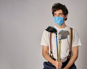 Golfer in casual clothing and with a protective covid-19 mask, he is holding some golf irons and a golf drive.