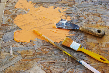 spatulas and brushes with orange paint for putty and repair