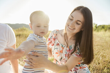 Happy mother with cute baby son enjoying summer sunlights on blanket in field