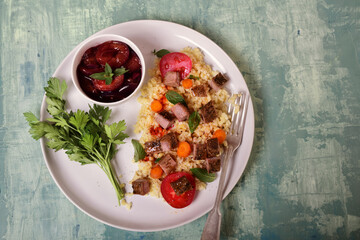 Meat salad on a white plate, pickled plums in a bowl