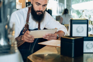Handsome Barista Doing an Inventory of the Products with Digital Tablet in a Cafe.

Serious waiter...