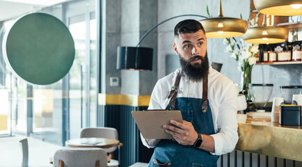Handsome Barista Doing an Inventory of the Products in a Coffee Shop.

Serious waiter with a beard...
