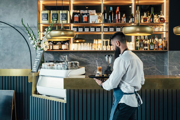 Handsome Waiter Carries Iced Coffee and Dessert on a Serving Tray. 
Professional barista preparing and bringing an order of latte coffee and slice of cake in a coffee shop.