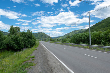 Fototapeta na wymiar highway road and mountain peaks on the background of a blue sky with clouds