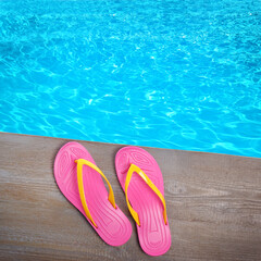 Pair of flip flops on wooden deck near swimming pool, top view
