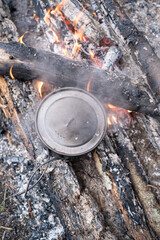 Pot of preparing food stands on the coals campfire, camp, summer day. Top view.