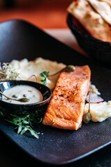 Salmon on puree on a black plate with white sauce