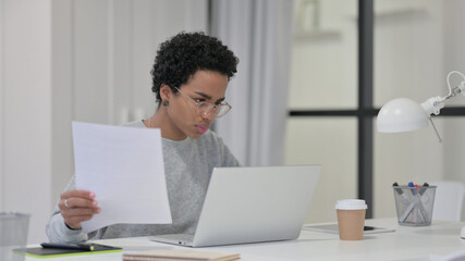 Fototapeta premium African Woman Reading Documents while using Laptop 