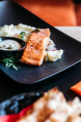 Salmon on puree on a black plate with white sauce
