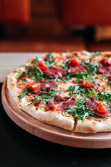 Pizza with cherry tomatoes, rucola and salami in bar environment