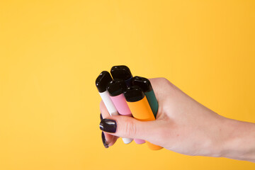 Hand holding vape sticks with a yellow background