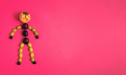 A human figure made of grape grains, plums and peach on pastel red background. Minimalistic creative funny autumn concept, flat lay composition