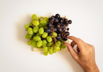A male hand takes a grape grain from the table. Minimal autumn harvest celebration concept on white...