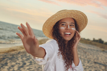 Happy African American woman with sun protection cream on face at beach