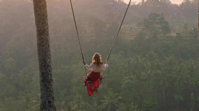 travel woman swinging over tropical rainforest at sunrise female tourist sitting on swing with scenic view enjoying freedom on vacation having fun holiday lifestyle slow motion