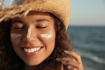 Happy African American woman with sun protection cream on face near sea, closeup