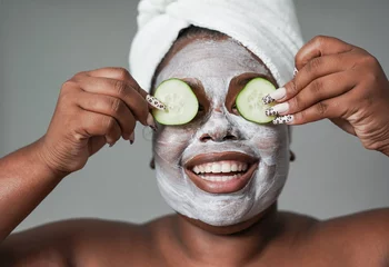 Keuken foto achterwand Young african woman with skin care cream holding fresh cucumber slices in front of her eyes - Beauty day and spa concept © Sabrina