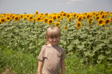 a happy boy with blond hair stands with in a field with sunflowers.