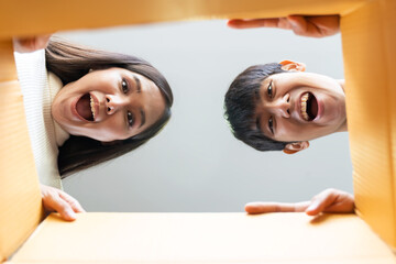 Cheerful Asian young couple opening cardboard box or parcel and looking inside