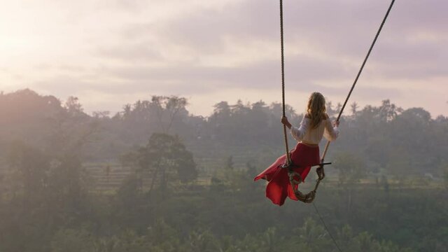 travel woman swinging over tropical rainforest at sunrise female tourist sitting on swing with scenic view enjoying freedom on vacation having fun holiday lifestyle slow motion