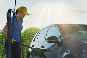 Woman in uniform cleaning car using high pressure water. Car wash service.