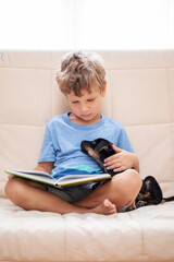 A boy with a little dog is reading a book