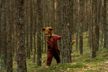 Toddler baby girl in bear bonnet walking in the woods
