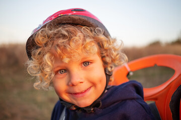White curly boy in a helmet in a bicycle seat - obrazy, fototapety, plakaty