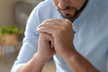 Religious man with clasped hands praying indoors, closeup