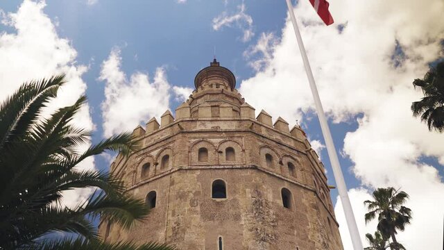 Torre de oro vista desde abajo y observando una bandera y un cielo lleno de nubes