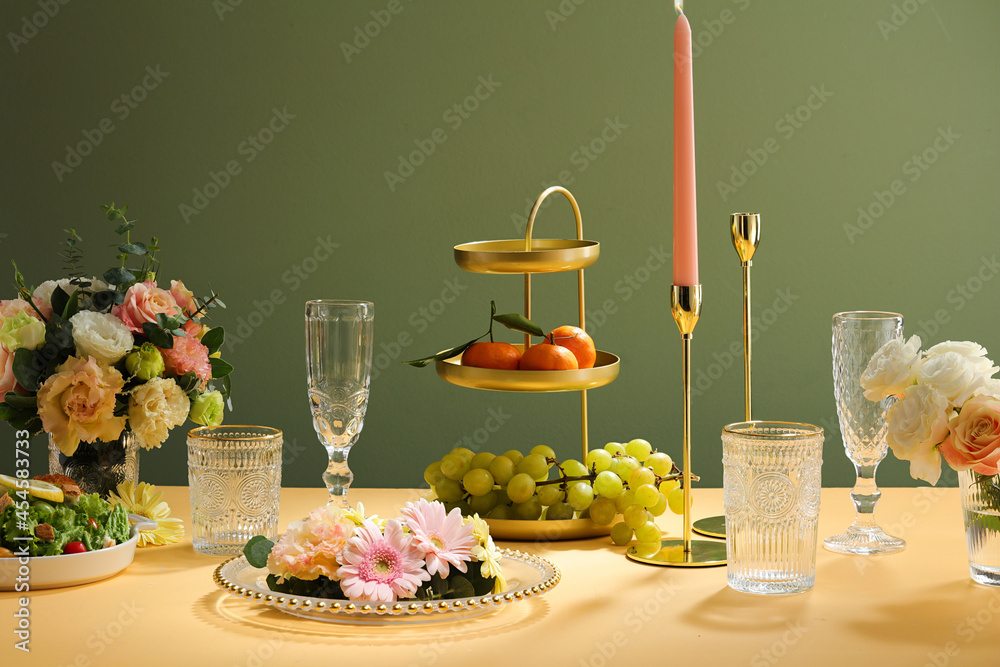 Wall mural wedding table setting with white plates and glass decorated with candles, green leaves, flower, tier