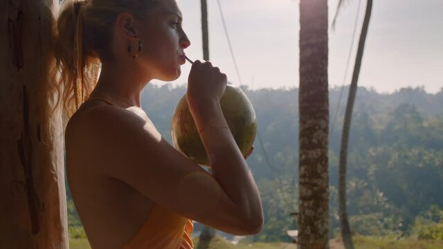 young travel woman drinking coconut cocktail at tropical hotel resort looking beautiful view of jungle enjoying exotic vacation lifestyle in paradise