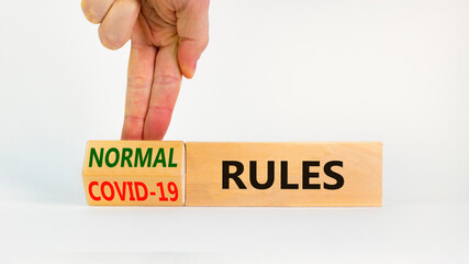 Symbol of covid-19 or normal rules. Doctor turns a wooden cube and changes words 'covid-19 rules'...