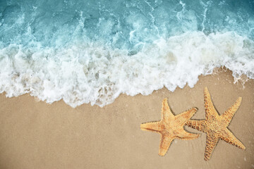 Fototapeta na wymiar Beautiful waves and sea stars on sandy beach, top view