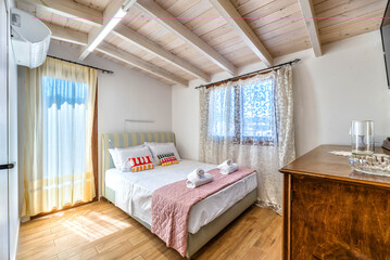 Country house sun lit bedroom with wooden ceiling, double bed. Floor made up of wood like parquet.