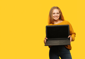 Blonde Woman Holding Laptop With Blank Screen over yellow background. Copy space.    Female holds...
