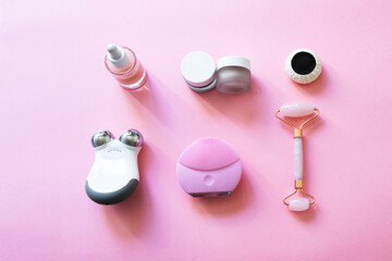 Modern beauty routine with gadgets. Cleanser and Microcurrent devices, Gua Sha roller, professional natural oil and creams on pink background
