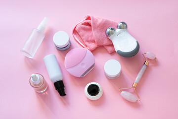 Obraz na płótnie Canvas Top view of cleanser and microcurrent devices, Gua Sha roller, professional cleansing cloths , natural oil and serum, cream and masks on pink background.Modern beauty skincare gadgets.