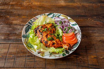 Chicken thigh cooked with Hindu tandoori recipe with parsley and tomato slices on vintage table