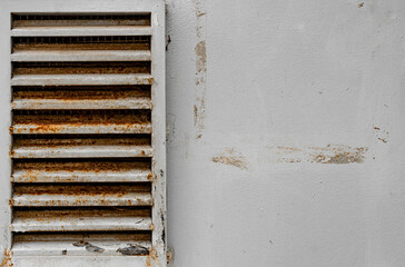 Dirty and rusty metal ventilation grill on a weathered gray wall.