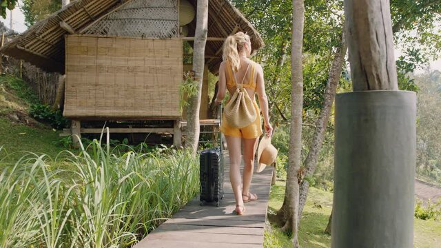 travel woman with trolly bag arriving at tropical hotel resort on exotic summer vacation walking to cottage